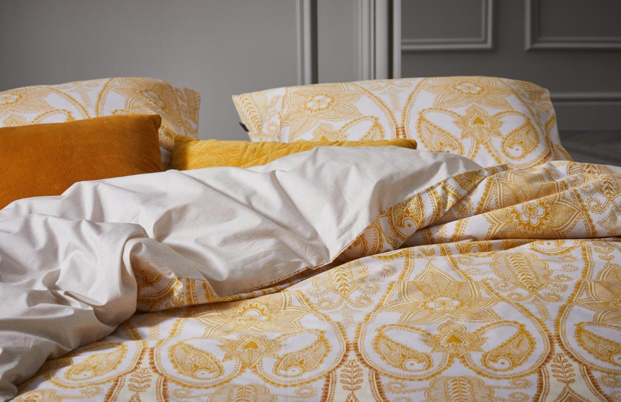 Auf einem Bett liegt ein Kopfkissen und eine Bettdecke bezogen mit Perkal Bettwaesche aus 100 Prozent Baumwolle mit Ornamenten in der Farbe Beige. Modell Dolley Vanilla.