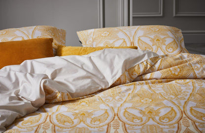 Auf einem Bett liegt ein Kopfkissen und eine Bettdecke bezogen mit Perkal Bettwaesche aus 100 Prozent Baumwolle mit Ornamenten in der Farbe Beige. Modell Dolley Vanilla.