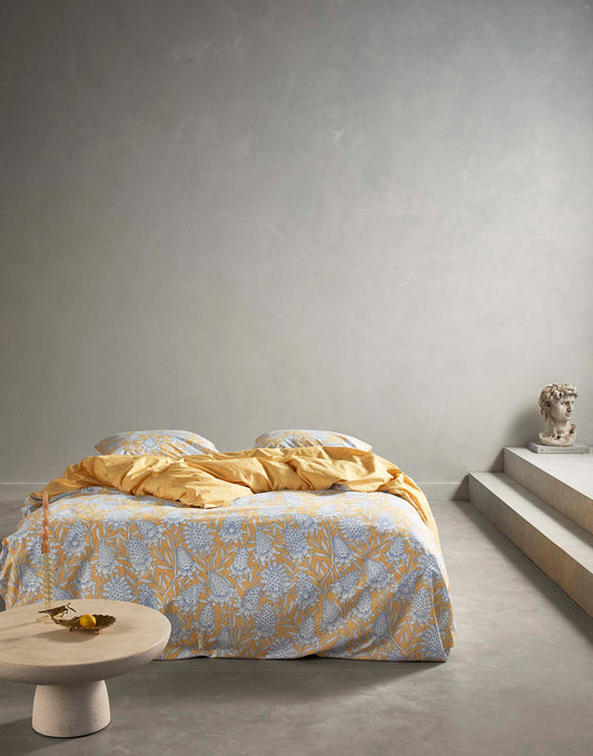 Ein Bettbezug-Set aus einem Kopfkissen und einer Bettdecke bezogen mit Perkal Bettwaesche aus 100 Prozent Baumwolle mit Muster aus Blumen in der Farbe Gelb. Modell Fela Sahara Sun.