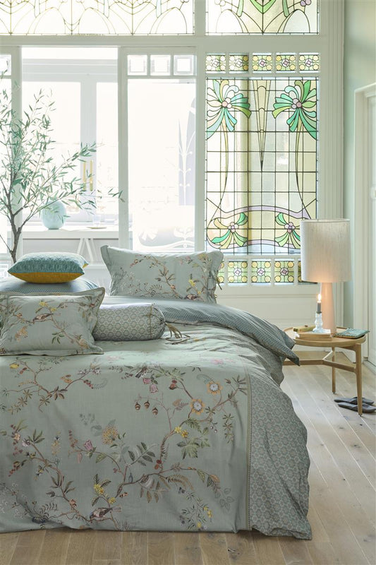 Auf einem Bett liegen mehrere Kopfkissen und eine Bettdecke bezogen mit Perkal-Baumwoll Bettwaesche aus 100 Prozent Baumwolle mit Muster aus Tieren und Pflanzen in der Farbe Blau. Modell Autunno Hellblau.