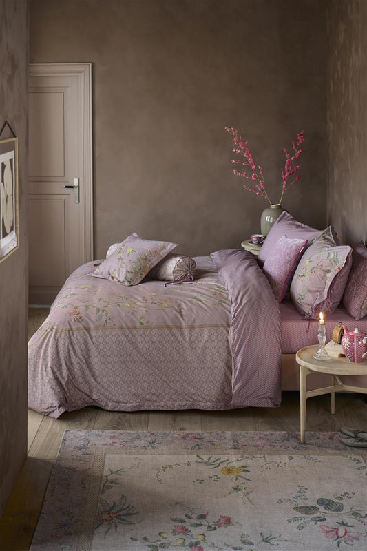 Auf einem Bett liegen mehrere Kopfkissen und eine Bettdecke bezogen mit Perkal-Baumwoll Bettwaesche aus 100 Prozent Baumwolle mit Muster aus Pflanzen und Tieren und grafischen Formen in der Farbe Lila. Modell Autunno Lila.