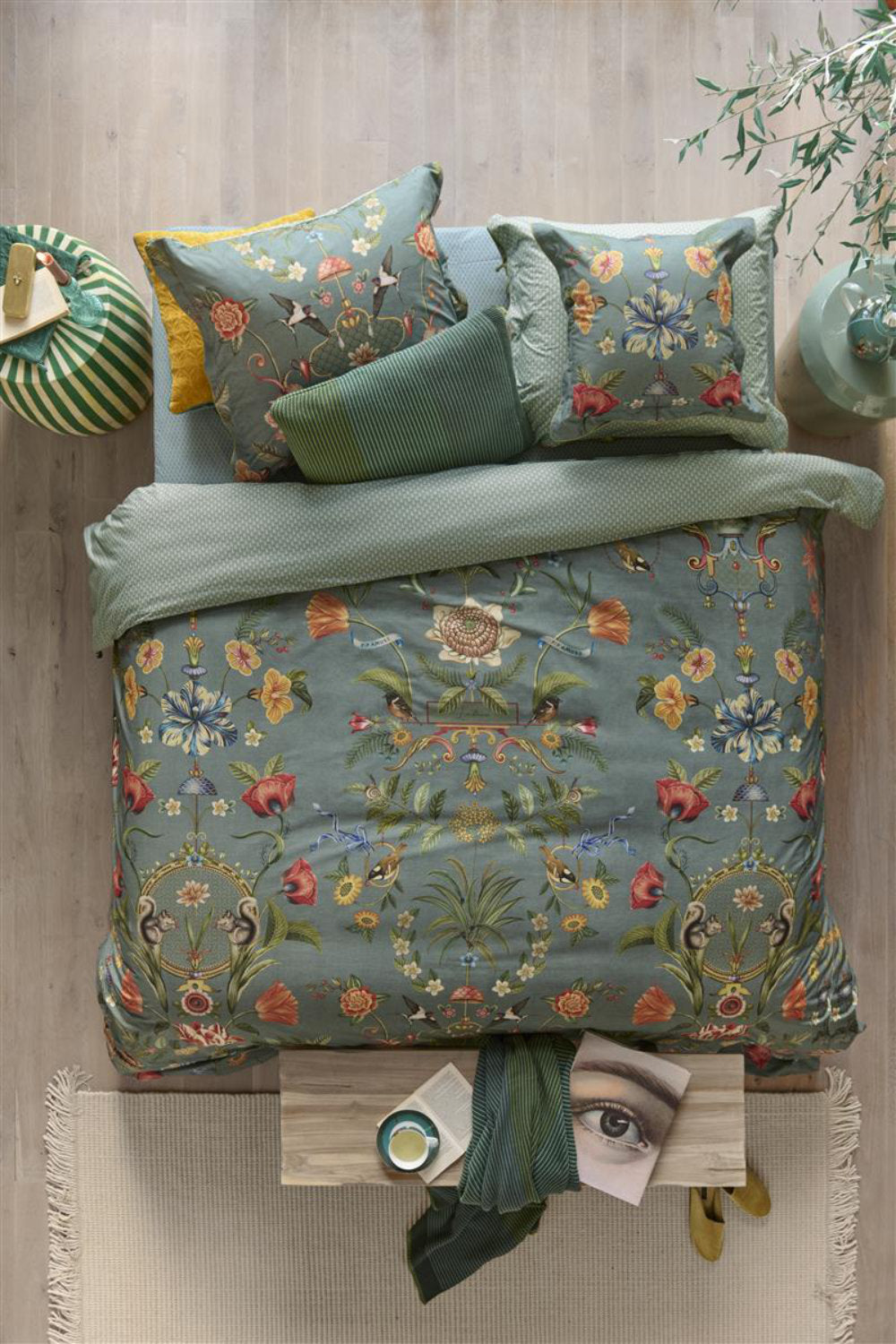 Auf einem Bett liegen mehrere Kopfkissen und eine Bettdecke bezogen mit Perkal-Baumwoll Bettwaesche aus 100 Prozent Baumwolle mit Muster aus Pflanzen und Tieren in der Farbe Petrol. Modell Botanico Verde Blau.