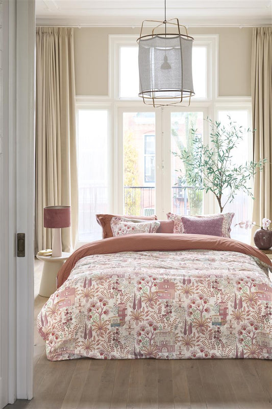 Auf einem Bett liegen mehrere Kopfkissen und eine Bettdecke bezogen mit Perkal-Baumwoll Bettwaesche aus 100 Prozent Baumwolle mit Muster aus Pflanzen und Gebauden und grafischen Formen in der Farbe Rosa. Modell Casa Di Pip Off-White.