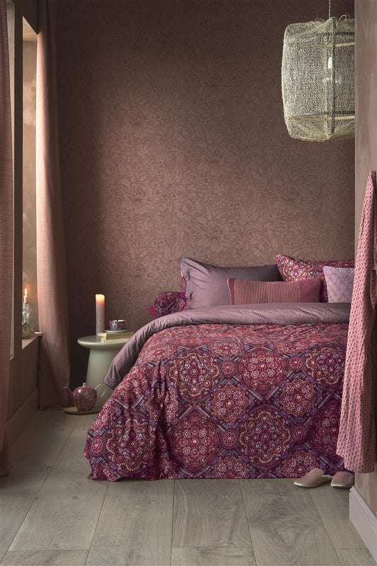 Auf einem Bett liegen mehrere Kopfkissen und eine Bettdecke bezogen mit Perkal-Baumwoll Bettwaesche aus 100 Prozent Baumwolle mit Muster aus Pflanzen in der Farbe Roségold. Modell Il Musaico Dark Red.