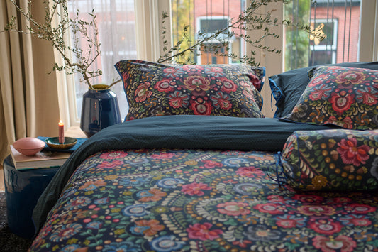 Auf einem Bett liegen mehrere Kopfkissen und eine Bettdecke bezogen mit Perkal-Baumwoll Bettwaesche aus 100 Prozent Baumwolle mit Muster aus Blumen in der Farbe Blau. Modell Il Ricamo Dark Blue.