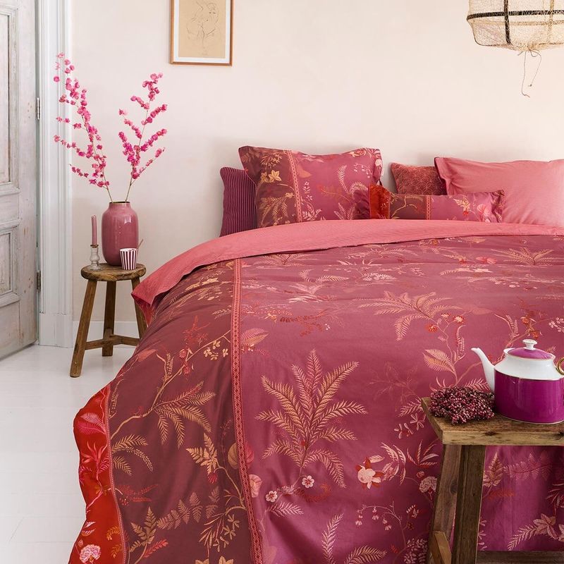 Auf einem Bett liegen mehrere Kopfkissen und eine Bettdecke bezogen mit Perkal-Baumwoll Bettwaesche aus 100 Prozent Baumwolle mit Muster aus Pflanzen in der Farbe Pink. Modell Isola Pink.
