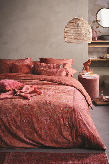 Auf einem Bett liegen mehrere Kopfkissen und eine Bettdecke bezogen mit Perkal-Baumwoll Bettwaesche aus 100 Prozent Baumwolle mit Muster aus Ornamenten in der Farbe Rot. Modell Kyoto Nights Pink.