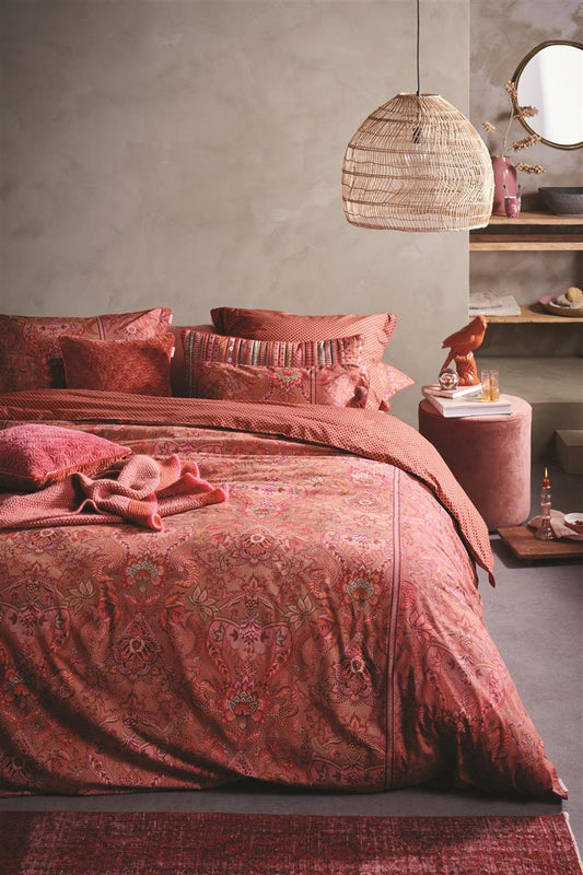 Auf einem Bett liegen mehrere Kopfkissen und eine Bettdecke bezogen mit Perkal-Baumwoll Bettwaesche aus 100 Prozent Baumwolle mit Muster aus Ornamenten in der Farbe Rot. Modell Kyoto Nights Pink.