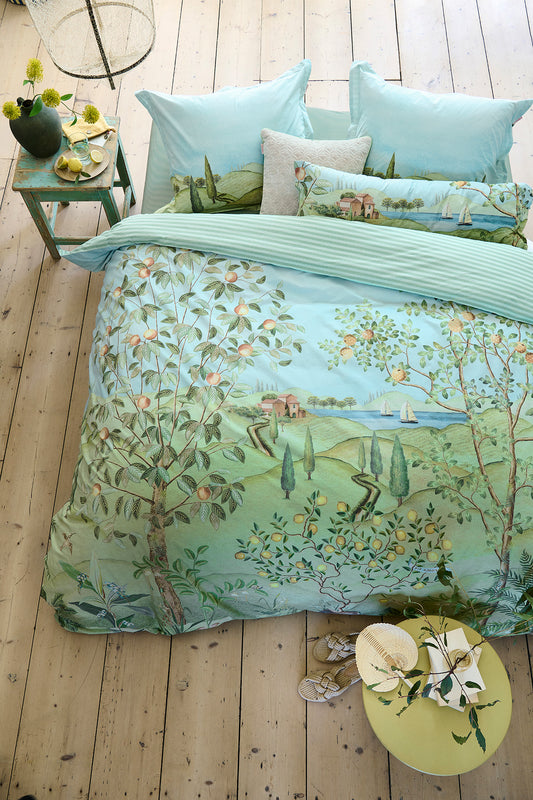 Auf einem Bett liegen mehrere Kopfkissen und eine Bettdecke bezogen mit Perkal-Baumwoll Bettwaesche aus 100 Prozent Baumwolle mit Muster aus einer Landschaft mit See und Baeumen in der Farbe Mint. Modell La Campagna Green.