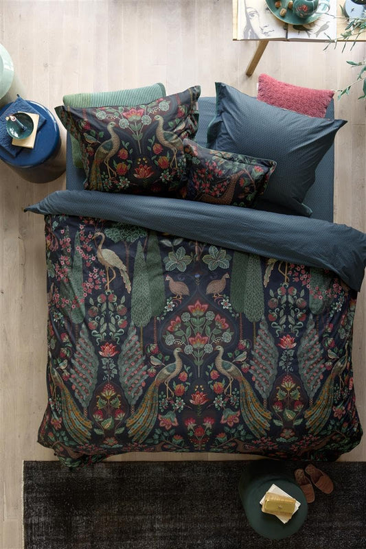 Auf einem Bett liegen mehrere Kopfkissen und eine Bettdecke bezogen mit Perkal-Baumwoll Bettwaesche aus 100 Prozent Baumwolle mit Muster aus Pflanzen und Voegeln in der Farbe Blau. Modell Pavoni Dunkelblau.