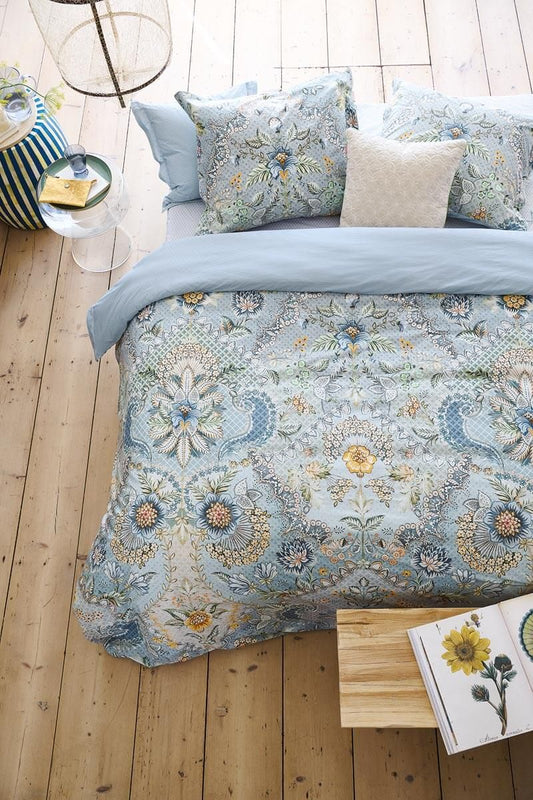 Auf einem Bett liegen mehrere Kopfkissen und eine Bettdecke bezogen mit Perkal-Baumwoll Bettwaesche aus 100 Prozent Baumwolle mit Muster aus Blumen in der Farbe Blau. Modell Saluti Grandi Hellblau.