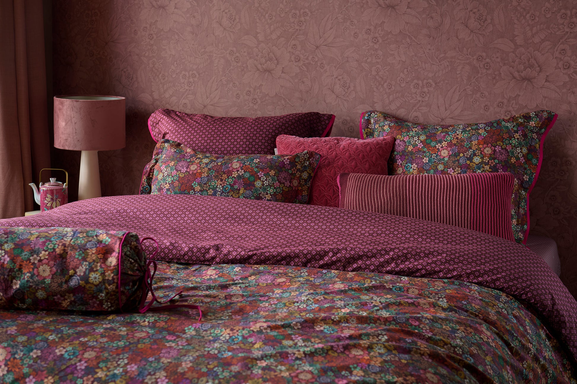 Auf einem Bett liegen mehrere Kopfkissen und eine Bettdecke bezogen mit Perkal-Baumwoll Bettwaesche aus 100 Prozent Baumwolle mit Muster aus Blumen in der Farbe Bordeaux. Modell Tutti i Fiori Dark Red.