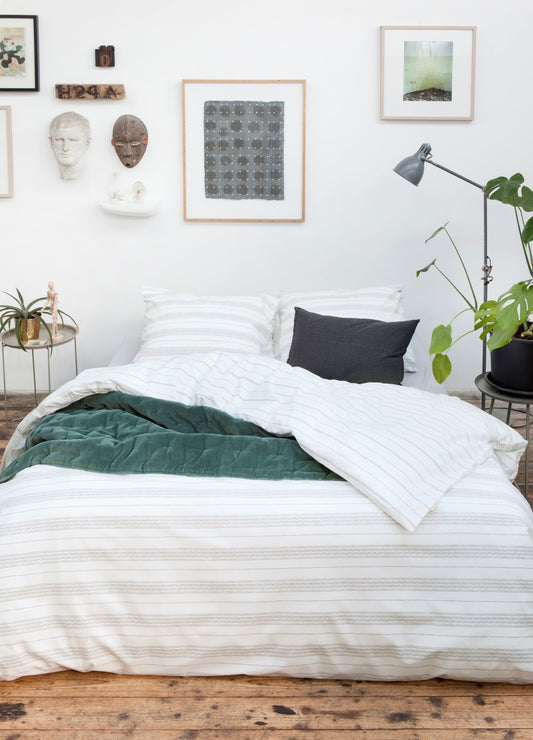 Auf einem Bett liegen mehrere Kopfkissen und eine Bettdecke bezogen mit Perkal-Baumwoll Bettwaesche aus 100 Prozent Baumwolle mit Muster aus horizontalen Streifen in der Farbe Weiss. Modell Head over Lines.