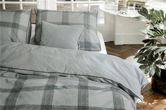 Auf einem Bett liegen mehrere Kopfkissen und eine Bettdecke bezogen mit Perkal-Baumwoll Bettwaesche aus 100 Prozent Baumwolle mit Muster aus Quadraten in der Farbe Grau. Modell Square Nights.