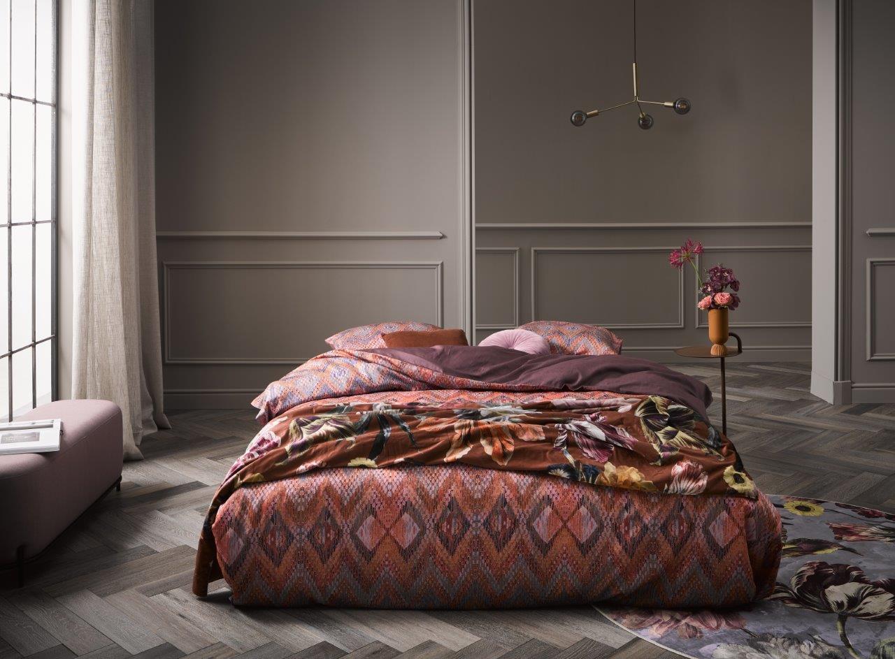 Ein Bettbezug-Set aus mehreren Kopfkissen und einer Bettdecke bezogen mit Satin Bettwaesche aus 100 Prozent Baumwolle mit Muster aus Linien in der Farbe Bordeaux. Modell Fabienne Terra.