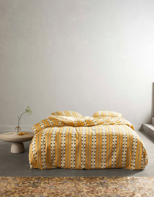 Ein Bettbezug-Set aus mehreren Kopfkissen und einer Bettdecke bezogen mit Satin Bettwaesche aus 100 Prozent Baumwolle mit Muster aus vertikalen Streifen in der Farbe Gelb. Modell Iva Ochre.