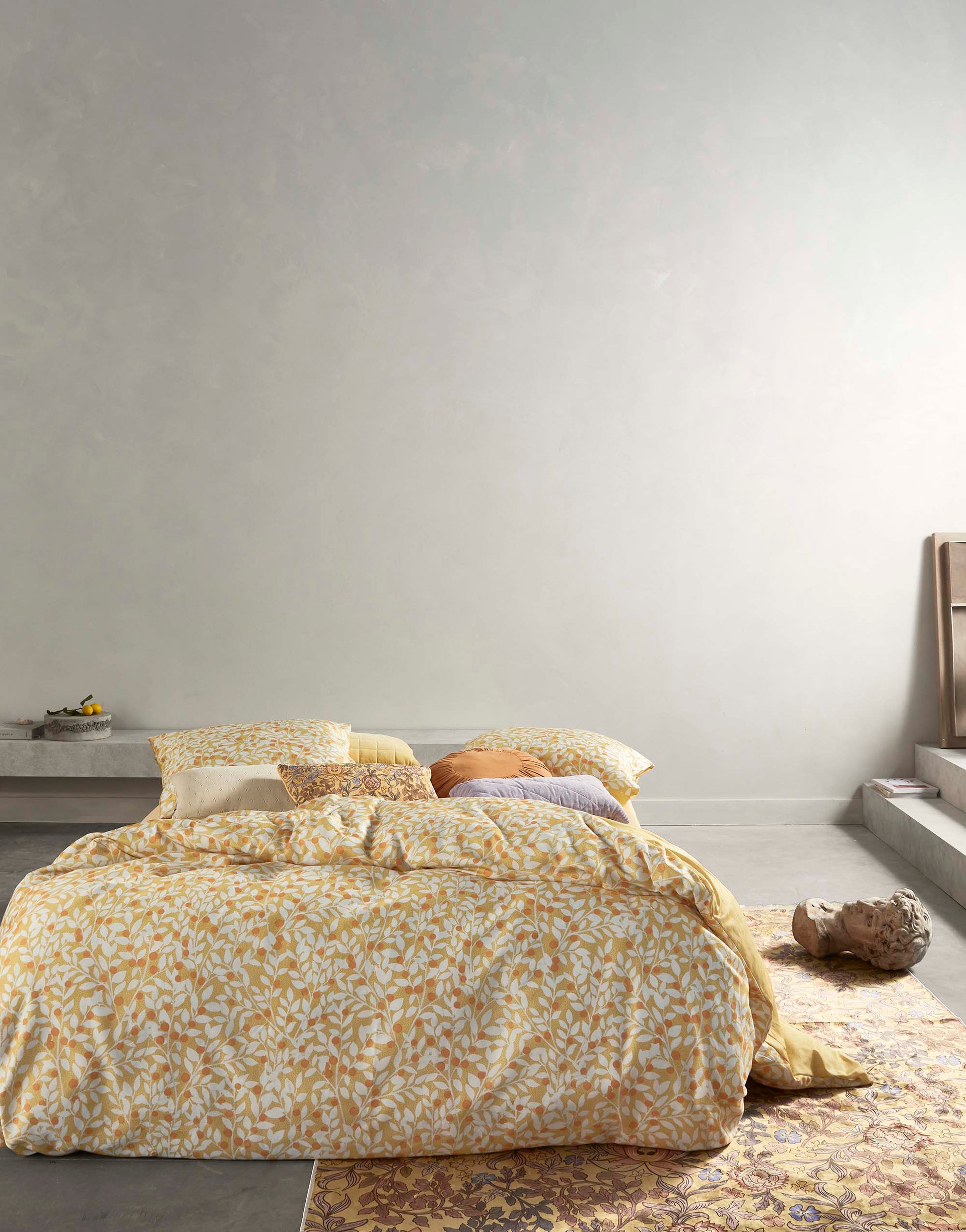 Ein Bettbezug-Set aus mehreren Kopfkissen und einer Bettdecke bezogen mit Satin Bettwaesche aus 100 Prozent Baumwolle mit Muster aus Zweigen in der Farbe Gelb. Modell Lenthe Sahara Sun.