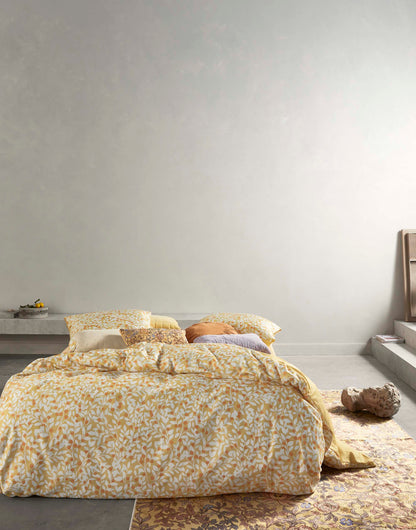 Ein Bettbezug-Set aus mehreren Kopfkissen und einer Bettdecke bezogen mit Satin Bettwaesche aus 100 Prozent Baumwolle mit Muster aus Zweigen in der Farbe Gelb. Modell Lenthe Sahara Sun.