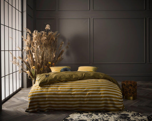 Ein Bettbezug-Set aus mehreren Kopfkissen und einer Bettdecke bezogen mit Satin Bettwaesche aus 100 Prozent Baumwolle mit Muster aus Linien und Quadraten in der Farbe Gelb. Modell Meg Ochre.