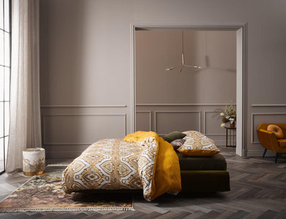 Ein Bettbezug-Set aus mehreren Kopfkissen und einer Bettdecke bezogen mit Satin Bettwaesche aus 100 Prozent Baumwolle mit Muster aus Ornamenten und Punkten in der Farbe Gelb. Modell Penelope Mustard.
