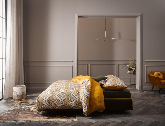 Ein Bettbezug-Set aus mehreren Kopfkissen und einer Bettdecke bezogen mit Satin Bettwaesche aus 100 Prozent Baumwolle mit Muster aus Ornamenten und Punkten in der Farbe Gelb. Modell Penelope Mustard.