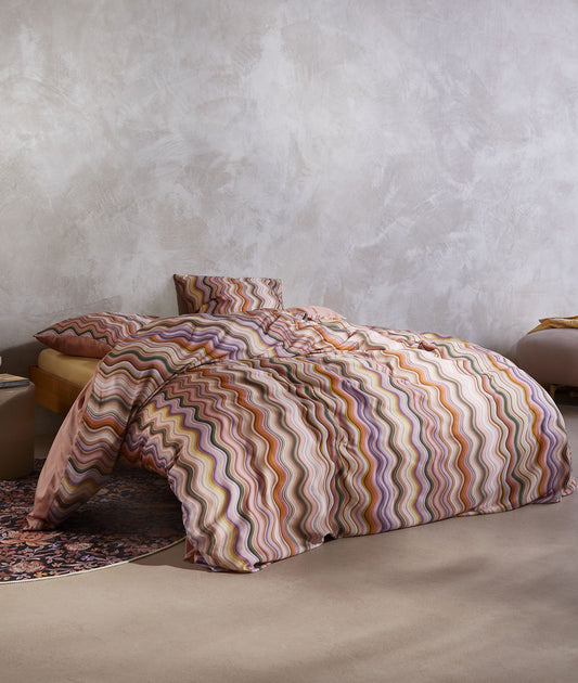 Ein Bettbezug-Set aus mehreren Kopfkissen und einer Bettdecke bezogen mit Satin Bettwaesche aus 100 Prozent Baumwolle mit Muster aus vertikalen Schlangenlinien in der Farbe Roségold. Modell Sol Antique Pink.