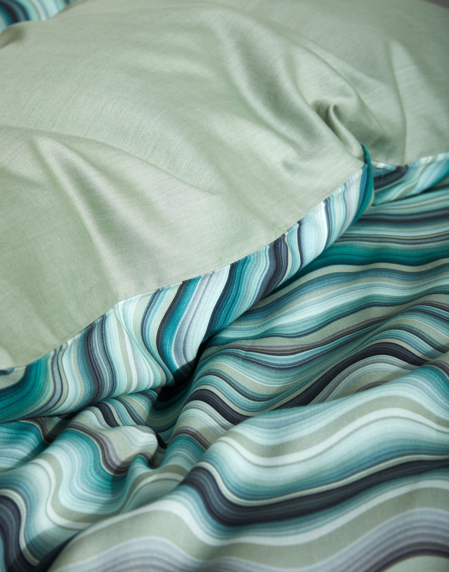 Detaildarstellung auf Kopfkissen und Bettdecke der Essenza Satin Bettwaesche Modell Sol Comforting Green.