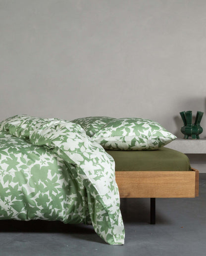 Ein Bettbezug-Set aus mehreren Kopfkissen und einer Bettdecke bezogen mit Satin Bettwaesche aus 100 Prozent Baumwolle mit Muster aus Blaettern in der Farbe Gruen. Modell Sora Greenish.