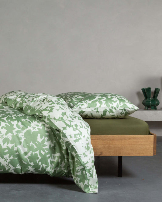 Ein Bettbezug-Set aus mehreren Kopfkissen und einer Bettdecke bezogen mit Satin Bettwaesche aus 100 Prozent Baumwolle mit Muster aus Blaettern in der Farbe Gruen. Modell Sora Greenish.