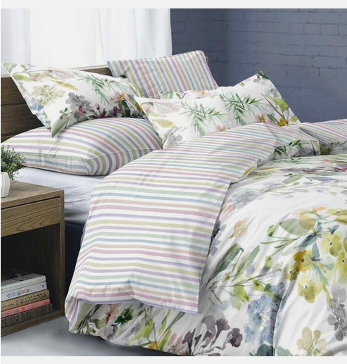 Auf einem Bett liegen mehrere Kopfkissen und eine Bettdecke bezogen mit Satin Bettwaesche aus 100 Prozent Baumwolle mit Muster aus Blumen und Streifen in der Farbe Mehrfarbig. Modell Clarendon Stripe.
