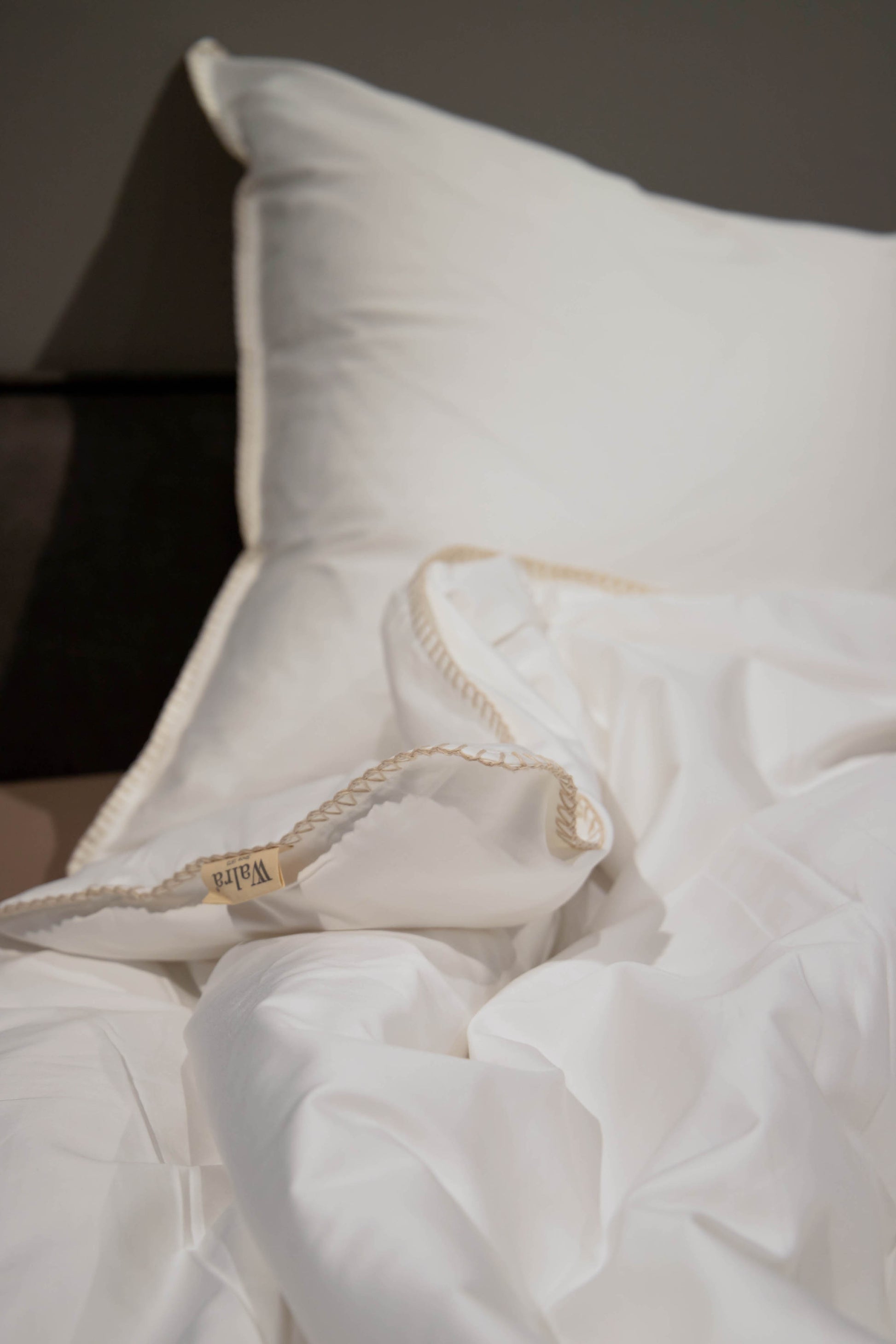 Auf einem Bett liegt ein Kopfkissen und eine Bettdecke bezogen mit Satin Bettwaesche aus 100 Prozent Baumwolle in der Farbe Weiss. Modell Fine Feston.