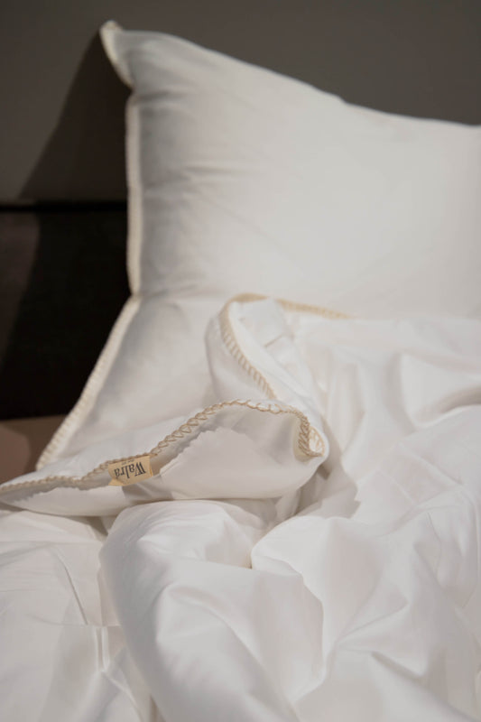 Auf einem Bett liegt ein Kopfkissen und eine Bettdecke bezogen mit Satin Bettwaesche aus 100 Prozent Baumwolle in der Farbe Weiss. Modell Fine Feston.
