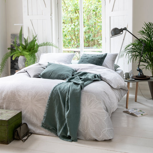 Auf einem Bett liegen mehrere Kopfkissen und eine Bettdecke bezogen mit Satin Bettwaesche aus 100 Prozent Baumwolle mit Muster aus Blueten in der Farbe Silber. Modell Fine Feston.