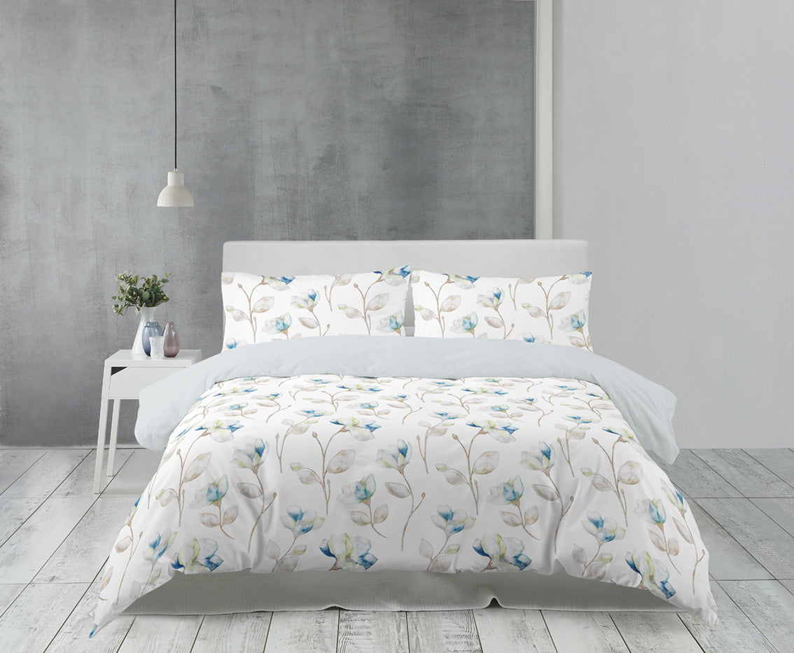Auf einem Bett liegen mehrere Kopfkissen und eine Bettdecke bezogen mit Satin Bettwaesche aus 100 Prozent Baumwolle mit Muster aus Blumen in der Farbe Weiss. Modell Florence White.