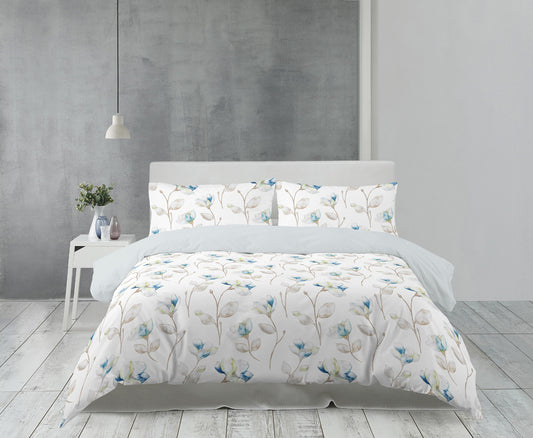 Auf einem Bett liegen mehrere Kopfkissen und eine Bettdecke bezogen mit Satin Bettwaesche aus 100 Prozent Baumwolle mit Muster aus Blumen in der Farbe Weiss. Modell Florence White.