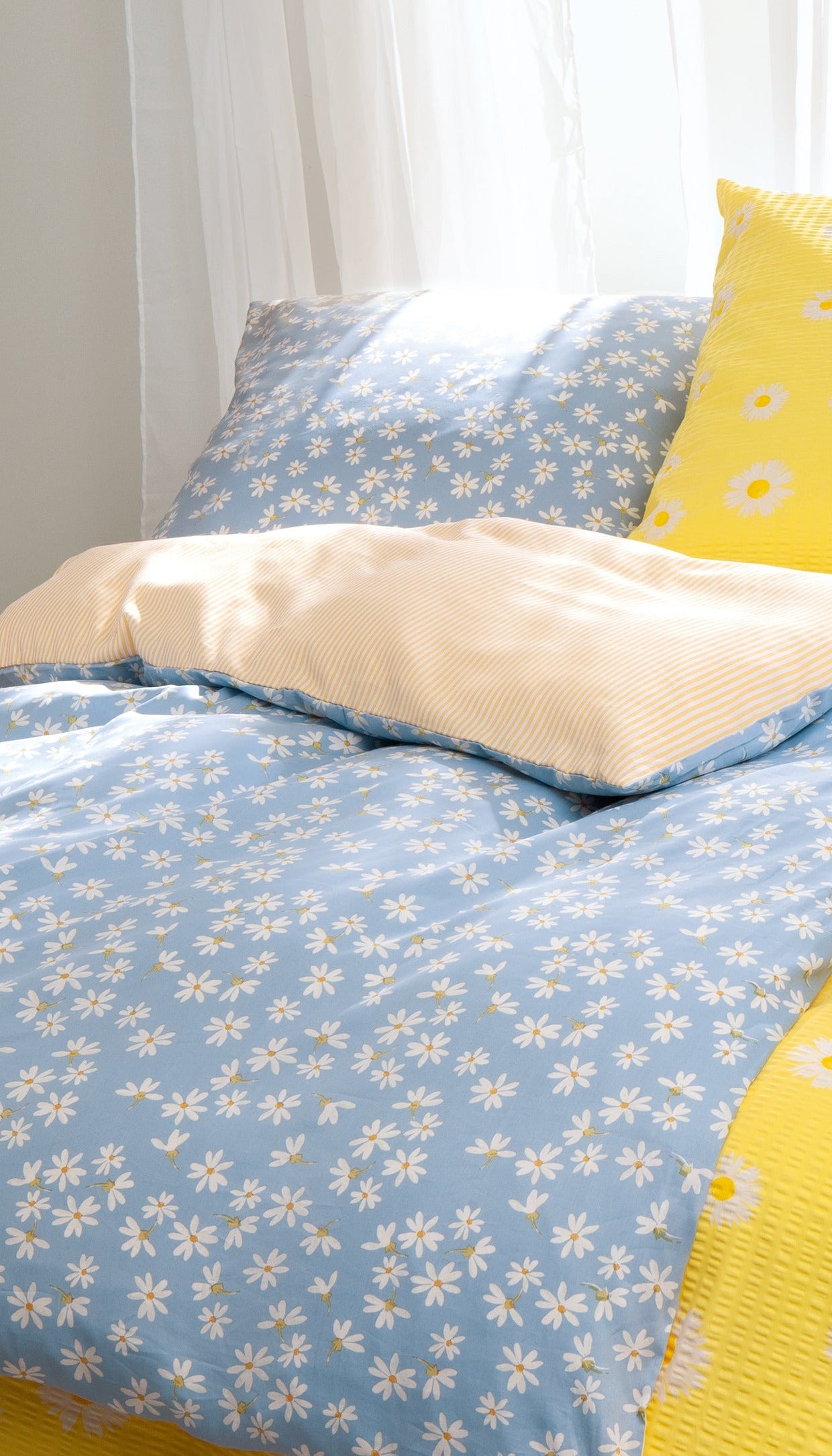 Auf einem Bett liegen mehrere Kopfkissen und eine Bettdecke bezogen mit Satin Bettwaesche aus 100 Prozent Baumwolle mit Muster aus Blumen in der Farbe Blau. Modell Kleine Blume.