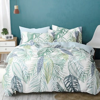 Auf einem Bett liegen mehrere Kopfkissen und eine Bettdecke bezogen mit Satin Bettwaesche aus 100 Prozent Baumwolle mit Muster aus Blaettern in der Farbe Mint. Modell Leaves.