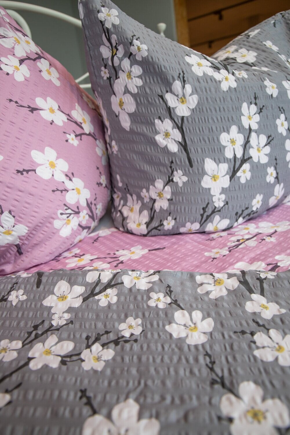 Ein Bettbezug-Set aus mehreren Kopfkissen und einer Bettdecke bezogen mit Satin-Seersucker Bettwaesche aus 100 Prozent Baumwolle mit Muster aus Blueten in der Farbe Grau. Modell Grau.