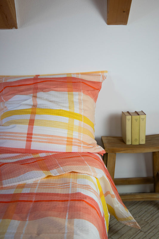 Ein Bettbezug-Set aus einem Kopfkissen und einer Bettdecke bezogen mit Seersucker Bettwaesche aus 100 Prozent Baumwolle mit Karomuster in der Farbe Orange. Modell Karo Orange.