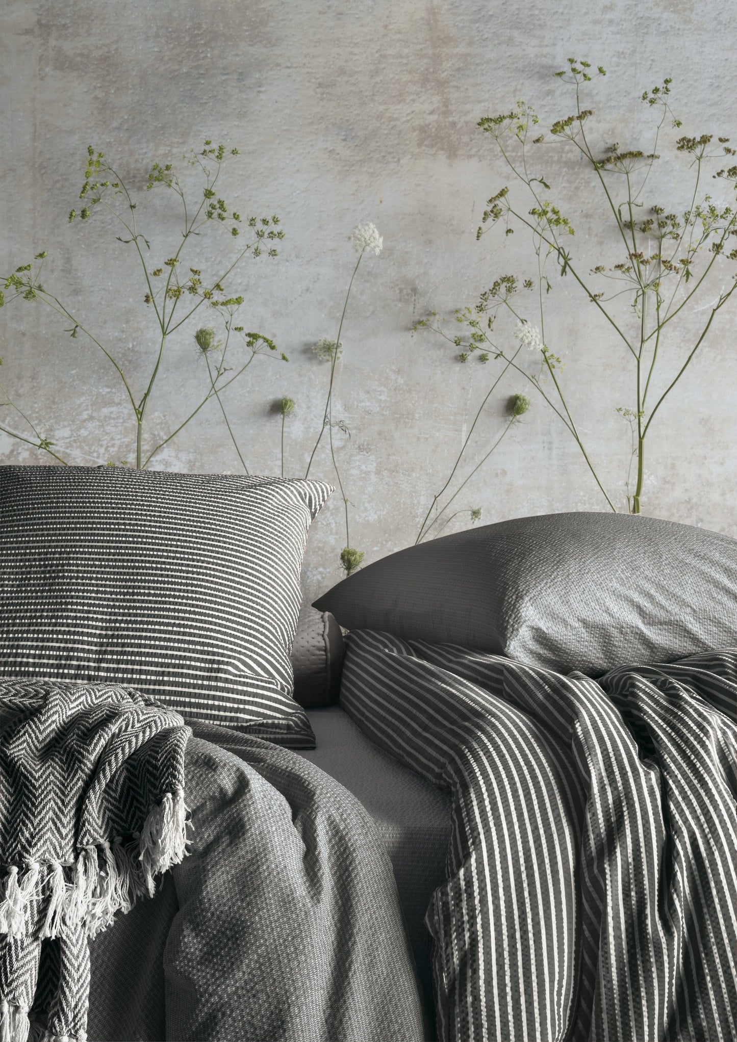 Ein Bettbezug-Set aus mehreren Kopfkissen und einer Bettdecke bezogen mit Soft Seersucker Bettwaesche aus 100 Prozent Baumwolle mit Muster aus Streifen in der Farbe Grau. Modell Easy Grey Stripe.