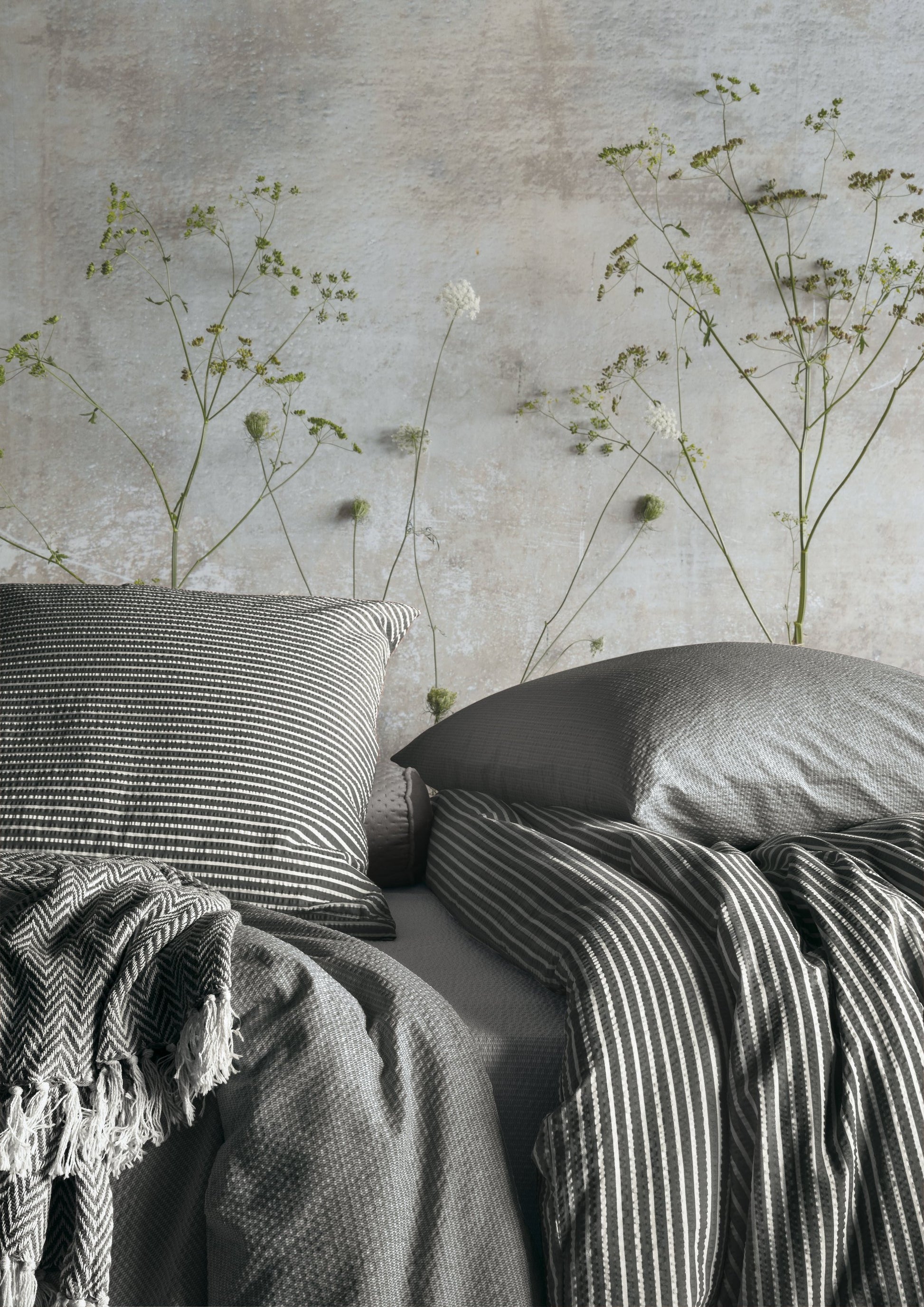 Ein Bettbezug-Set aus mehreren Kopfkissen und einer Bettdecke bezogen mit Soft Seersucker Bettwaesche aus 100 Prozent Baumwolle mit Muster aus Streifen in der Farbe Grau. Modell Easy Grey Stripe.