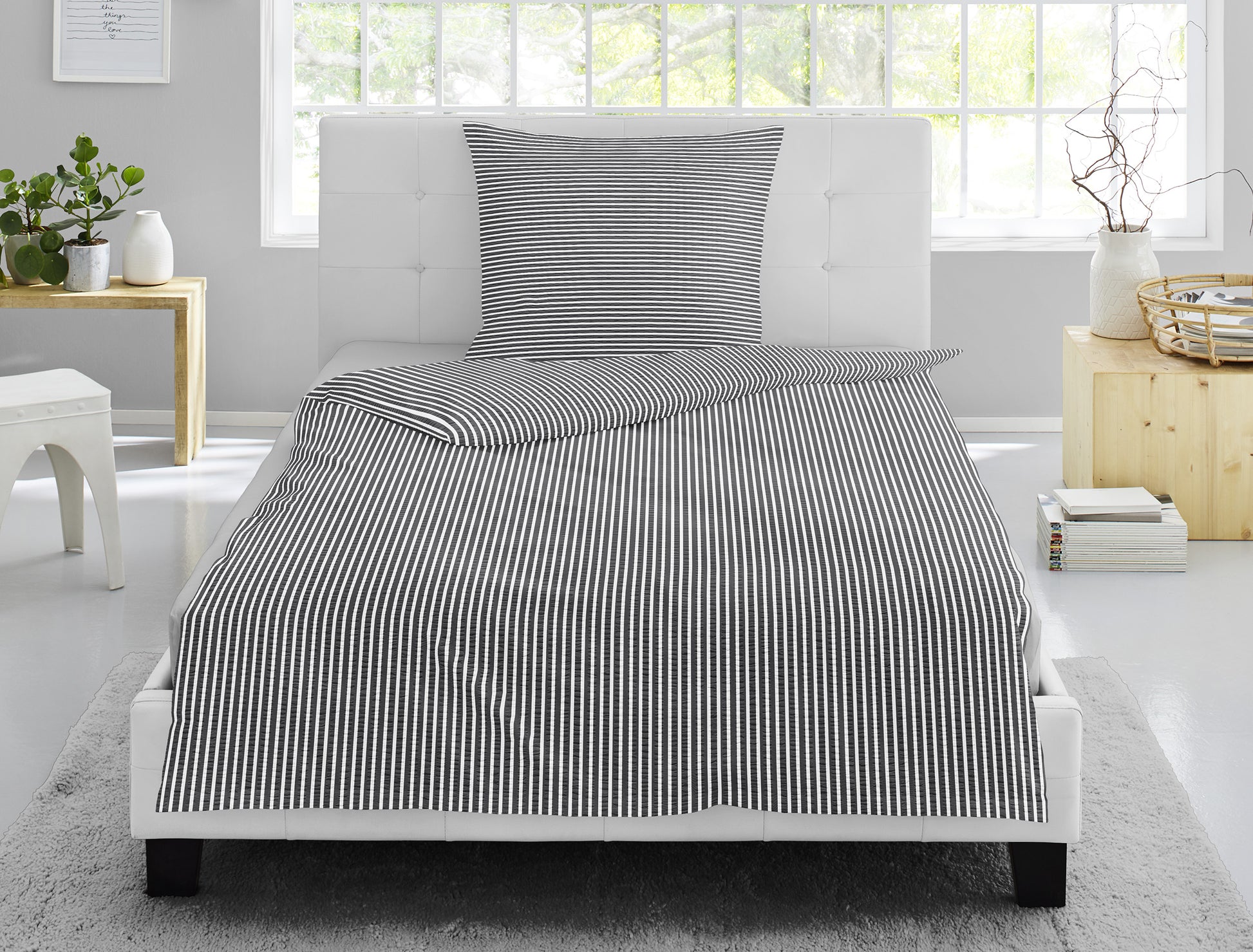 Auf einem Bett liegt ein Kopfkissen und eine Bettdecke bezogen mit Soft Seersucker Bettwaesche aus 100 Prozent Baumwolle mit Muster aus Streifen in der Farbe Grau. Modell Easy Grey Stripe.