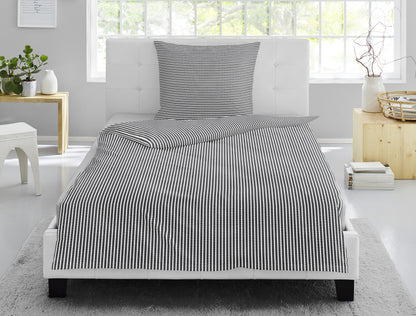 Auf einem Bett liegt ein Kopfkissen und eine Bettdecke bezogen mit Soft Seersucker Bettwaesche aus 100 Prozent Baumwolle mit Muster aus Streifen in der Farbe Grau. Modell Easy Grey Stripe.