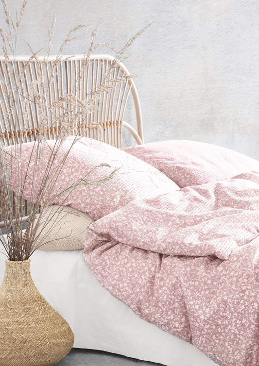 Auf einem Bett liegen mehrere Kopfkissen und eine Bettdecke bezogen mit Soft Seersucker Bettwaesche aus 100 Prozent Baumwolle mit Muster aus Blaettern in der Farbe Rosa. Modell Easy-Leave Rosa.