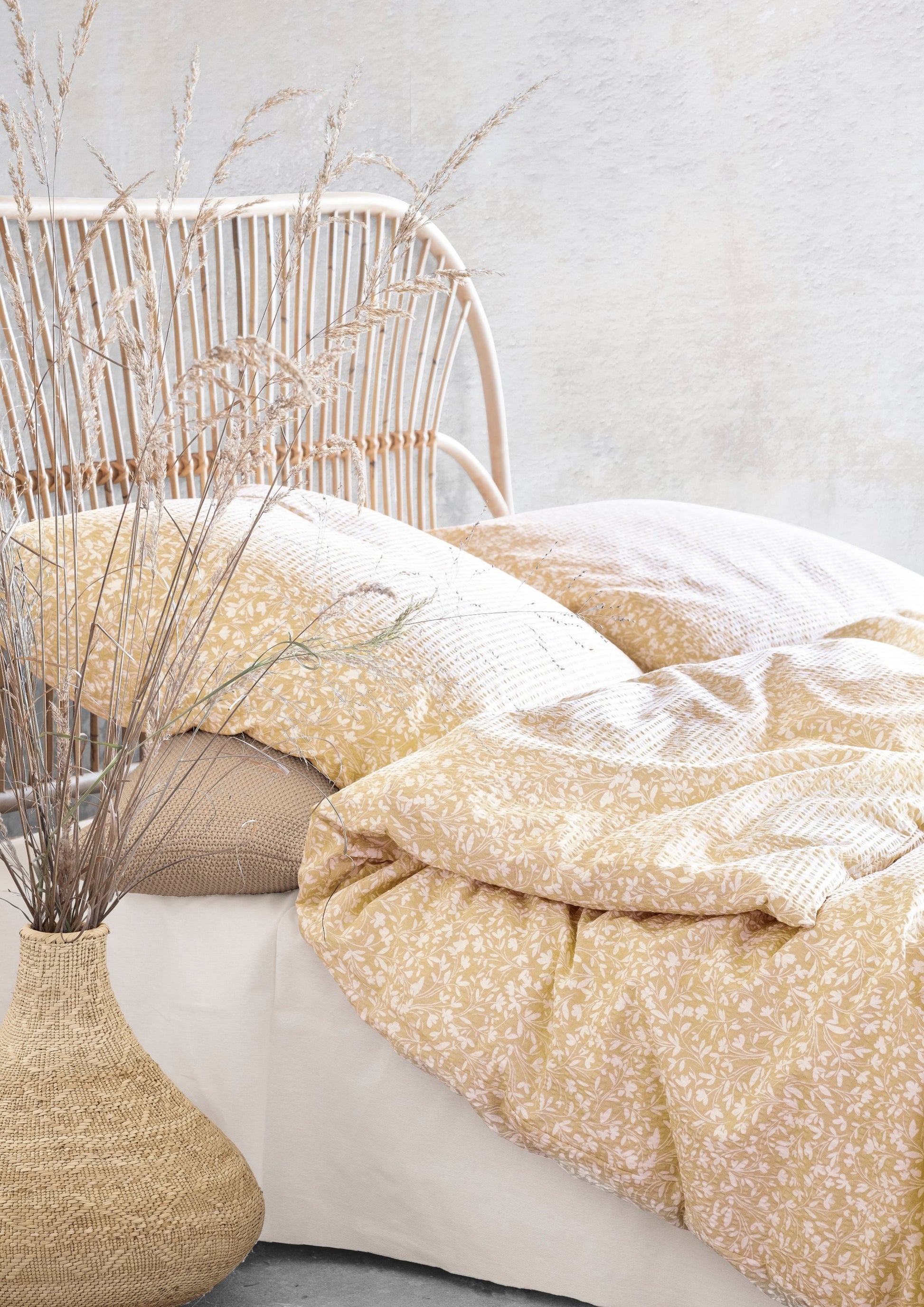 Auf einem Bett liegen mehrere Kopfkissen und eine Bettdecke bezogen mit Soft Seersucker Bettwaesche aus 100 Prozent Baumwolle mit Muster aus Blaettern in der Farbe Gelb. Modell Easy-Leave Yellow.