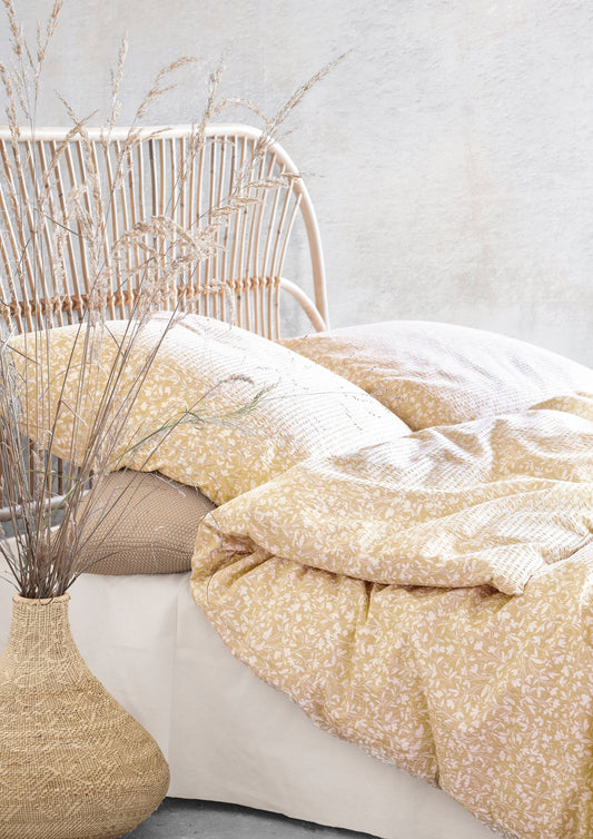 Auf einem Bett liegen mehrere Kopfkissen und eine Bettdecke bezogen mit Soft Seersucker Bettwaesche aus 100 Prozent Baumwolle mit Muster aus Blaettern in der Farbe Gelb. Modell Easy-Leave Yellow.
