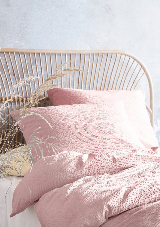 Auf einem Bett liegen mehrere Kopfkissen und eine Bettdecke bezogen mit Soft Seersucker Bettwaesche aus 100 Prozent Baumwolle in der Farbe Rosa. Modell Easy Rosa.