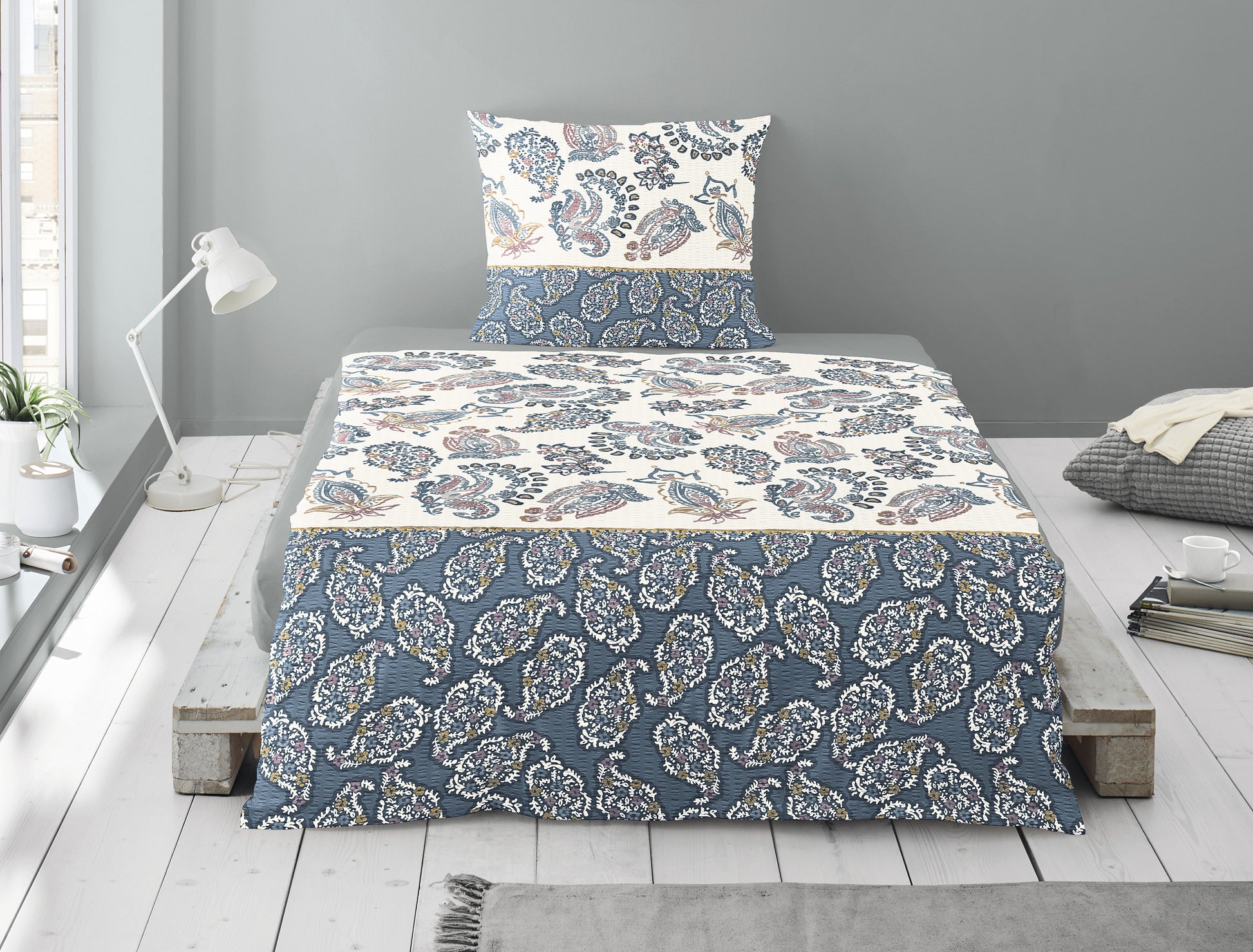 Auf einem Bett liegt ein Kopfkissen und eine Bettdecke bezogen mit Soft Seersucker Bettwaesche aus 100 Prozent Baumwolle mit Muster aus Ornamenten in der Farbe Blau. Modell Shadow Blue.