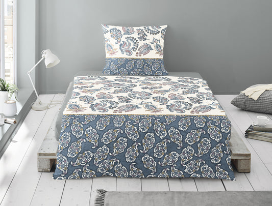 Auf einem Bett liegt ein Kopfkissen und eine Bettdecke bezogen mit Soft Seersucker Bettwaesche aus 100 Prozent Baumwolle mit Muster aus Ornamenten in der Farbe Blau. Modell Shadow Blue.