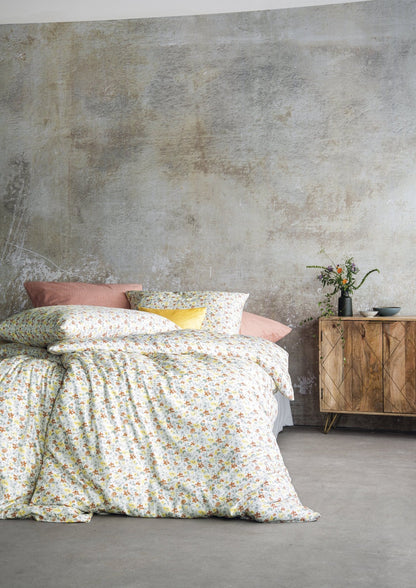 Auf einem Bett liegen mehrere Kopfkissen und eine Bettdecke bezogen mit Soft Seersucker Bettwaesche aus 100 Prozent Baumwolle mit Muster aus Blumen in der Farbe Gelb. Modell Shadow Multi.
